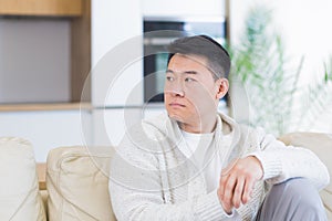 Bored friends young asian man sitting on sofa at home alone. Misses male sitting on the couch in apartment. Lonely guy indoors