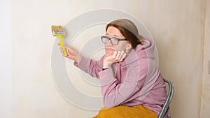 A bored girl lazily smears the wall with wallpaper paste. The concept of tired of doing repairs yourself