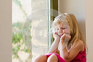 Bored girl with long blond hair sitting by the window