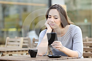 Bored girl looking at her smart phone on a cafe