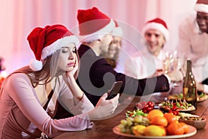 Bored Girl Using Smartphone Celebrating Xmas With Friends At Home