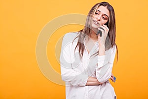 Bored girl in white shirt talking on the phone and holding credit card over yellow background