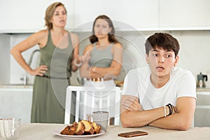 Bored guy is sitting at kitchen and unwittingly listens to mothers altercation with adult daughter photo