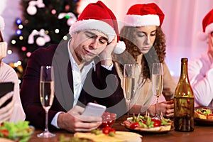Bored Guy Using Smartphone During Christmas Party With Friends Indoor