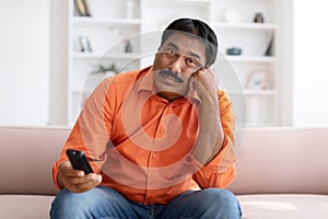 Bored Indian Man Watching TV Switching Channels With Remote Control