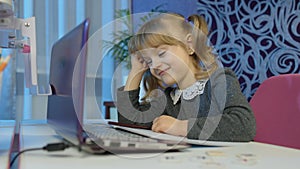 Bored kid listening audio lesson studying at table using digital laptop computer, doing homework