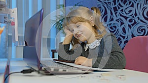 Bored kid listening audio lesson studying at table using digital laptop computer, doing homework