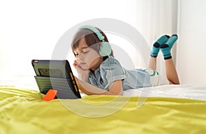 Bored little boy looking at tablet with sad face lying down on sofa looking deep in thought