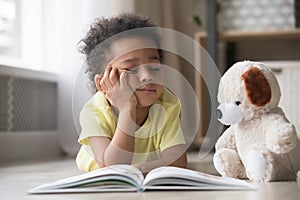 Bored little boy reading book lying on floor