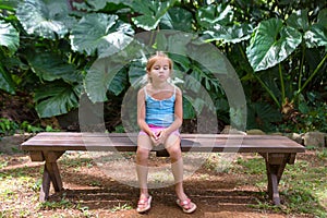 Bored little girl sitting on a bench in paradise