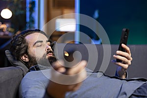 Bored man lounged on couch binging series and texting on phone