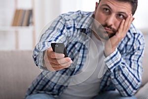 Bored man with remote control watching TV at home