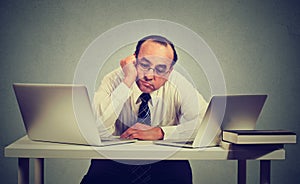 Bored man sitting in front of two laptop computers