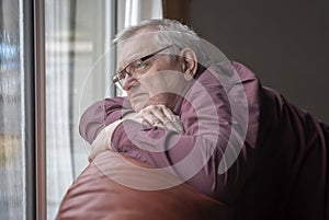 Bored man in sixties looking out the window in home