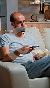 Bored man switching TV channels, holding popcorn in hads