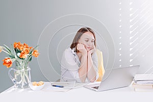 Bored middle age woman sitting at desktop table working on laptop, computer. Tired young woman learning online on Internet. Work