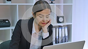 Bored office worker at desk staring at computer screen with hand on chin