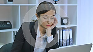 Bored office worker at desk staring at computer screen with hand on chin
