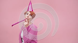 Bored red haired middle aged woman blowing party horn on the birthday party. Purple colors