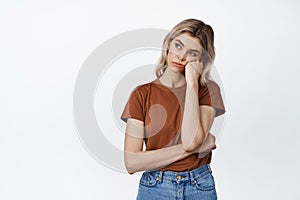 Bored and sad girl looking left, lean head on fist with skeptical, moody face expression, standing over white background