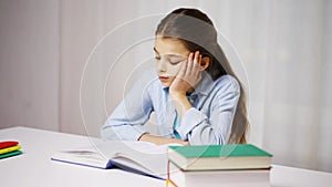 Bored school girl reading book or textbook at home