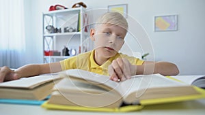 Bored schoolboy doing homework and reading books, upset kid touching head