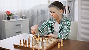 Bored schoolboy playing chess and looking at watch, unwilling to continue