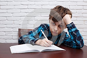 Bored schoolboy writing down a task into a notebook. Studying di