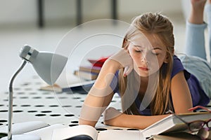 Bored schoolgirl doing homework while lying on floor indoors