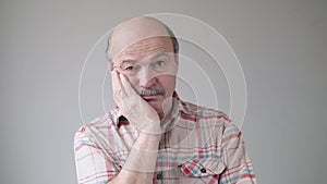 Bored senior hispanic man holding hand on his cheek has gloomy and sad emotion on his face.