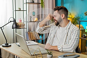 Bored sleepy businessman worker working on laptop rubbing eye pinch nose, pain headache at office