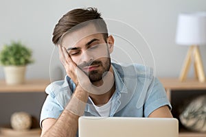 Bored sleepy man feels drowsy resting on hand near laptop