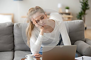 Bored sleepy woman holding head on hand, sitting with laptop