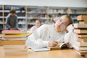 Bored teenage girl trying to prepare for exam in library