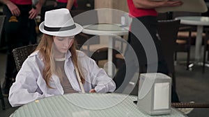 Bored teenage girl wearing hat while sitting at restaurant