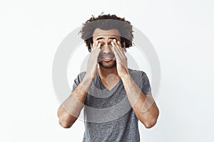 Bored tired african man touching face with hands over white background.