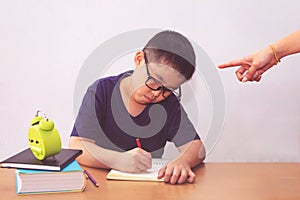 Bored and tired asian student boy doing homework. Angry mother pointing with him