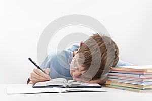 Bored and tired boy doing homework on desk. Schoolboy fell asleep on notebook. Home schooling