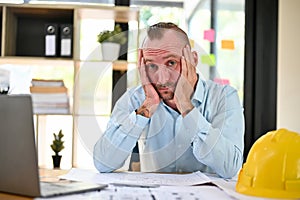 Bored and tired caucasian male engineer hands on his chin, looking at the camera