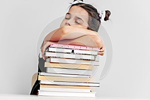 Bored and tired schoolgirl sleeping on a pile of books on the desk against light grey background. Exhausted little girl learner