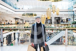 A bored and tired senior man with paper bags in shopping centre at Christmas time.