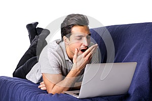 Bored or tired young man yawning while working on laptop computer