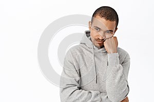 Bored or uspet young man, lean head on arm and looking disappointed, gloomy at camera, standing over white background