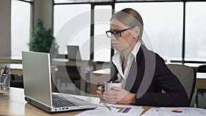 Bored woman having coffee break in office, dissatisfied with work, lack of ideas