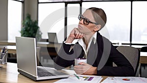 Bored woman having coffee break in office, dissatisfied with work, lack of ideas