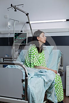 Bored woman recieving iv drip line treatment sitting on bedside looking into distance