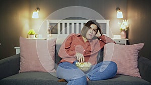 Bored woman sitting on the sofa, eating popcorn and watching TV