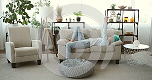 Bored woman using mobile phone lying upside down on sofa at home