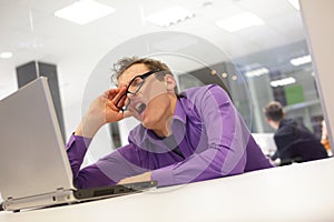 Bored yawning businessman working with laptop photo