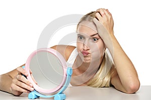 Bored young blond woman looking at herself in the mirror